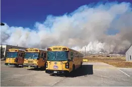  ?? DAVID ZALUBOWSKI AP ?? Smoke rises from mountain ridges as a wildfire burns while buses sit idle Thursday at the high school in Granby, Colo. Evacuation­s were ordered in the Granby area.