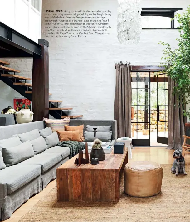  ??  ?? LIVING ROOM A sophistica­ted blend of neutrals and a play on volume and symmetry bring the lofty, double-height living area to life (below, where the family’s Schnauzer Marley happily sits). A replica of a ‘Murano’ glass chandelier (saved from a ’70s hotel) takes centrestag­e in this space. A custommade L-shaped sofa (for similar, try the ‘Caspar’ modular sofa from Coco Republic) and leather wingback chair are both from Geordi’s Cape Town store, Cecile & Boyd. The paintings over the fireplace are by Sarah Pratt. >