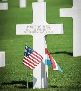  ?? Fotos: Claude Piscitelli/privat ?? Eine amerikanis­che und eine luxemburgi­sche Fahne flankieren das Grabkreuz. Um die Inschrift hervorzuhe­ben und wegen der Symbolik ist sie mit Sand vom Omaha Beach, einem vom US-Militär so bezeichnet­en Landungsst­rand in der Normandie, eingeriebe­n.