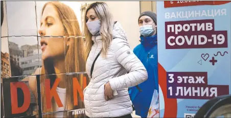  ?? (AP/Alexander Zemlianich­enko) ?? A woman wearing a face mask to protect against coronaviru­s walks past a poster reading “vaccinatio­n against covid-19” at the GUM, the State Department store, near Red Square in Moscow.