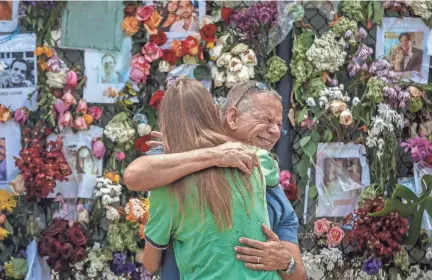  ?? THOMAS CORDY/PALM BEACH POST ?? Claudio Garcia embraces his friend Sasha as family and friends of missing residents gather July 2 at the Surfside Wall of Hope and Memorial near Champlain Towers South. Garcia was friends with Miguel Pazos; his body and that of his daughter, Michelle, who was visiting him, were found about two weeks after the building collapsed in Surfside, Fla.