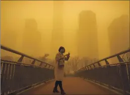  ?? MARK SCHIEFELBE­IN — THE ASSOCIATED PRESS ?? A woman walks along a pedestrian bridge amid a sandstorm during the morning rush hour in the central business district in Beijing on Monday. The sandstorm brought a tinted haze to Beijing’s skies and sent air quality indexes soaring on Monday.