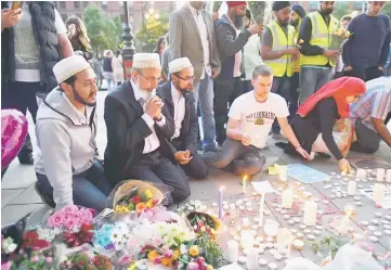  ?? — AFP photo ?? People pray and light candles set up in front of floral tributes in Albert Square in Manchester, northwest England, in solidarity with those killed and injured in the May 22 terror attack at the Ariana Grande concert at the Manchester Arena.