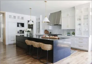  ?? AIMEE MAZZENGA — FRESH TWIST STUDIO ?? A kitchen design with woven Palecek kitchen stools and a striking midnight blue stone island to balance the extensive Shaker-style white and glass cabinetry. The brass-toned lining of the pendant fixtures from Circa Lighting is echoed in the cabinet hardware.