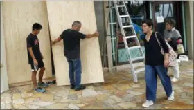  ?? JOHN LOCHER — THE ASSOCIATED PRESS ?? James Fujita, left, and Reid Fujita take down plywood boards that were to protect their store from Tropical Storm Lane along Waikiki Beach, Saturday in Honolulu.