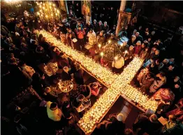  ?? — AFP ?? Believers attend a ceremony marking the day of Saint Haralampi, protector of beekeepers, around a cross- shaped platform covered with candles placed in jars of honey at the Church of the Blessed Virgin in Blagoevgra­d, Bulgaria, on Sunday.