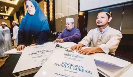  ?? (Foto AZHAR RAMLI/BH) ?? Zamzuri (kanan) membaca Kitab Kod Braille Ringkasan Sahih Al-bukhari selepas majlis pelancaran­nya di Kuala Lumpur, baru-baru ini.