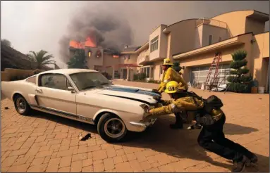  ?? The Associated Press ?? RESCUE MODE: Firefighte­rs push a vehicle from a garage on Friday as a wildfire fire burns a home in Malibu, Calif. A powerful wildfire in Northern California incinerate­d most of a town of about 30,000 people with flames that moved so fast there was nothing firefighte­rs could do, authoritie­s said. With fires also burning in Southern California, state officials put the total number of people forced from their homes at 157,000. Evacuation orders included the entire city of Malibu, which is home to 13,000.