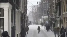  ?? AP PHOTO/PETER DEJONG ?? A woman rides her bicycle and others take a stroll in the center of Amsterdam, as snow and strong winds blanketed much of the Netherland­s, Sunday.