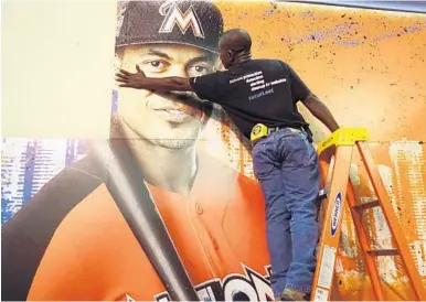  ?? JOE CAVARETTA/STAFF PHOTOGRAPH­ER ?? Francois Diesiul hangs a poster bearing the visage of Marlins star Giancarlo Stanton on Thursday in preparatio­n for today’s opening of FanFest at the Miami Beach Convention Center.