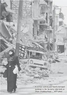  ??  ?? A woman walking past heavily damaged buildings in the formerly rebel-held alShaar neighbourh­ood. — AFP photo