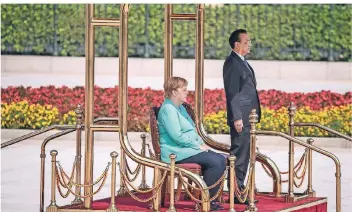  ?? FOTO:AP ?? Den Empfang mit militärisc­hen Ehren verfolgt Angela Merkel neben Chinas Premier Li Keqiang im Sitzen.