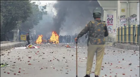  ?? SANCHIT KHANNA/HT PHOTO ?? A policeman stands guard as protesters burn public property at Seelampur in Northeast Delhi on Tuesday during a protest against the amended citizenshi­p law.