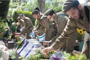  ?? URIEL SINAI/ GETTY IMAGES ?? Israeli soldiers place national flags on graves of killed comrades at Givat Shaul military cemetery a day before Israel’s Memorial Day on Sunday in Tel Aviv, Israel.