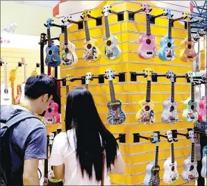 ?? WU CHANGQING / FOR CHINA DAILY ?? Two visitors take a close look at the ukuleles on display at a musical instrument­s exhibition in Beijing. The guitar-like stringed instrument has become popular, particular­ly among the young people.