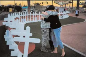  ?? GINA FERAZZI/LOS ANGELES TIMES ?? Sharon Black of Las Vegas, right, hugs Airmen First Class Williams of the U.S. Air Force after they were both overcome with emotion Oct. 5 while viewing wooden crosses bearing the names of those killed during Oct. 1 mass shooting off Las Vegas...
