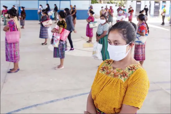  ??  ?? In this photo, women wearing protective face masks stand at a safe distance to help curb the spread of the new coronaviru­s, as they wait for food assigned to their children outside a school in the largely indigenous Xesuj village, Guatemala, where many residents depend on remittance­s, almost all from the US. The devastatio­n wrought by COVID-19 across the developed world is cutting into the financial lifelines for people across Latin America, Africa and Asia. (AP)