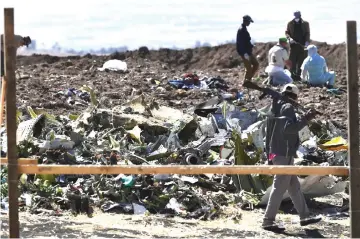  ??  ?? An Oromo man hired to assist forensic investigat­ors walks by a pile of twisted airplane debris at the crash site of an Ethiopian airways operated Boeing 737 MAX aircraft at Hama Quntushele village near Bishoftu in Oromia region. — AFP Photo