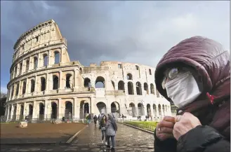  ?? Alberto Pizzoli / AFP via Getty Images ?? A man wearing a protective mask passes by the Coliseum in Rome on Saturday amid fear of the COVID-19 epidemic.