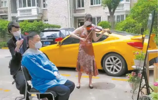  ?? ?? Liu Lijie plays the violin while Su Ran gives Liu Bingqiang a haircut in a neighborho­od in Shanghai’s Changning District. — Ti Gong