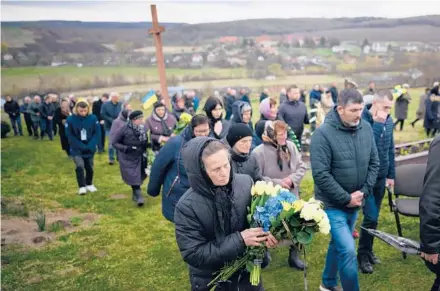  ?? LEON NEAL/GETTY ?? People walk through a cemetery ahead of the funeral for a fallen soldier on Saturday in Dev’yatnyky, Ukraine.