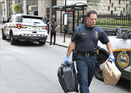  ?? Darrell Sapp/ Post- Gazette ?? A Pittsburgh police officer carries evidence that was collected from a bus stop Downtown where two women were stabbed. One of the women later died at the hospital.