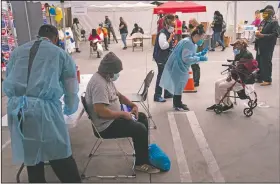  ?? (AP/Jae C. Hong) ?? Viola Roberson (far right), 75, and 61-year-old Mark McNamee (foreground) wait for their covid-19 vaccine at a vaccinatio­n site set up in the parking lot of the Los Angeles Mission in the Skid Row area of Los Angeles.