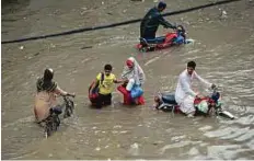  ?? AFP ?? Residents wade through a flooded street following heavy rain in Lahore yesterday.