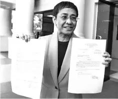  ??  ?? Ressa shows the warrant of arrest order after posting bail at a court in Manila. — AFP photo