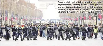  ?? — AFP photo ?? French riot police take position in front of protesters wearing yellow vests (gilets jaunes) demonstrat­ing against rising costs of living they blame on high taxes on the Champs-Elysees in Paris.