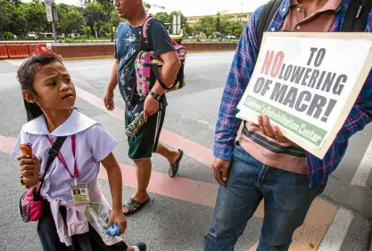  ?? —JAMSTA. ROSA ?? INNOCENT WITNESS A schoolgirl in Quezon City walks past one of the protesters against the House bill amending the country’s juvenile justice system by lowering the minimum age of criminal responsibi­lity (MACR) from 15 years to 9. The measure was approved by the House committee on justice on Monday.