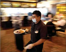  ?? DAVID J. PHILLIP, FILE — THE ASSOCIATED PRESS ?? A server wears a face mask as he delivers food to a table at Picos restaurant in Houston.