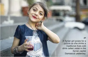  ?? AP ?? A Syrian girl poses for a picture as she drinks a traditiona­l Arab cold drink called Jallab in the Syrian capital Damascus yesterday.