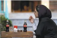  ?? Ebrahim Noroozi / Associated Press ?? A woman at a Tehran cafe smokes a Marlboro cigarette at a table with two Cokes, all U.S.made goods.