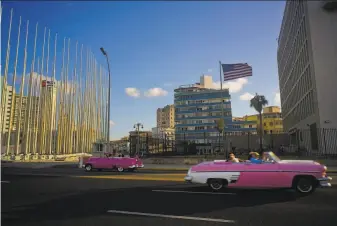  ?? Ramon Espinosa / Associated Press 2017 ?? Tourists ride in classic American convertibl­es in 2017 past the United States Embassy (right) in Havana. President Biden is taking initial steps toward restoring closer relations with Cuba.