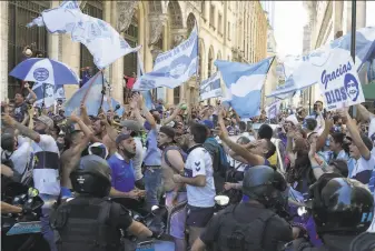  ?? Federico Peretti / Getty Images ?? Fans wave flags as police attempt to contain them while they wait to file past the coffin of soccer star Diego Maradona in Buenos Aires. The nation declared three days of mourning.