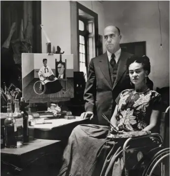  ?? © FRIDA KAHLO MUSEUM ?? Frida Kahlo is shown in this photo with her surgeon, Dr. Juan Farill, taken by Gisèle Freund in 1951. In the background is Kahlo’s painting “Self-Portrait with the Portrait of Doctor Farill” (1951). The photograph is one of many included in a new exhibit at the National Museum of Mexican Art in Pilsen.