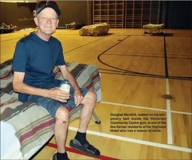  ?? JOE FRIES/Penticton Herald ?? Douglas Nendick, seated on his temporary bed inside the Penticton Community Centre gym, is one of the few former residents of the Highland Motel who has a reason to smile.