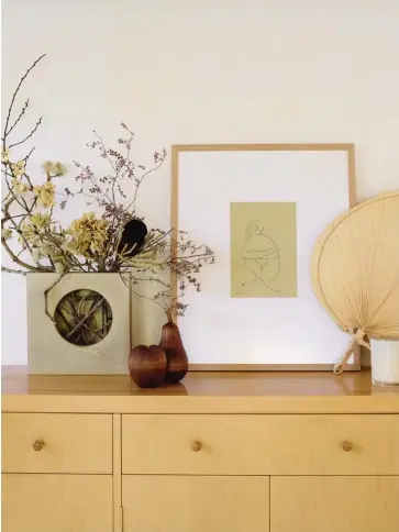  ??  ?? ABOVE On this pre-loved sideboard near the dining area, an ikebana vase is filled with a bespoke f loral arrangemen­t created by Here Among The Wild. The George Sand Studio print is from Endemic World, and the wooden fruit and paper fan were from a favourite Instagram store that’s since closed. OPPOSITE Erena found the kitchen’s 1967 “witch hat” Semi pendant lights by Fog and Mørup on Etsy. The Daily Roller on the left wall is by George &amp; Willy, the stools were a Trade Me discovery and the ceramics on the peg-board shelves crafted by Charles were all made by local potters.