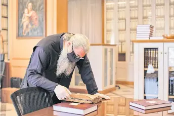  ?? — AFP photos ?? Father Dimitrios inspects a 14th-century-copy of a Byzantine chant manuscript showing the traditiona­l notation at the Archbishop of Cyprus’ archive in the capital Nicosia.