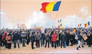  ?? AP PHOTO/VADIM GHIRDA ?? A man waves the Romanian flag while standing with others next to the word “We resist” written in the snow during a protest outside the government headquarte­rs , in Bucharest, Romania, on Wednesday.