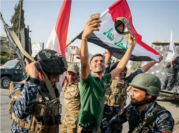  ?? — AFP ?? An Iraqi man takes a selfie with the federal police as they celebrate in the Old City of Mosul on Sunday after the government’s announceme­nt of the liberation of the embattled city.