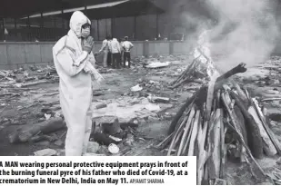  ?? Ap/amit Sharma ?? A man wearing personal protective equipment prays in front of the burning funeral pyre of his father who died of Covid-19, at a crematoriu­m in new Delhi, India on may 11.