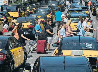  ?? LLUIS GENE / AFP ?? Turistas arrastrand­o maletas por una Gran Via de Barcelona ocupada por los taxis