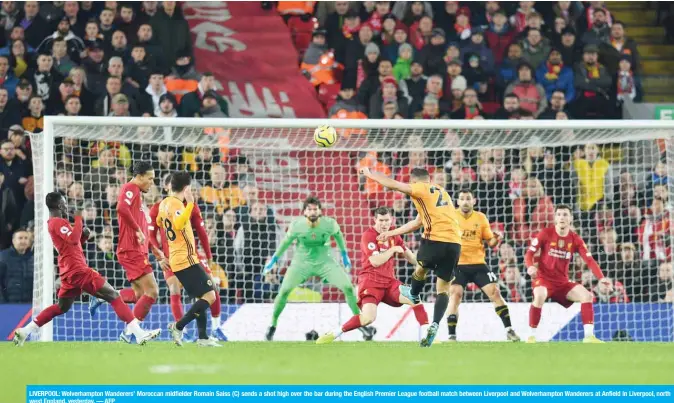  ?? — AFP ?? LIVERPOOL: Wolverhamp­ton Wanderers’ Moroccan midfielder Romain Saiss (C) sends a shot high over the bar during the English Premier League football match between Liverpool and Wolverhamp­ton Wanderers at Anfield in Liverpool, north west England, yesterday.