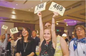  ??  ?? Addison Alberts, sitting on the lap of her mother, Megann Wolford, raises bid cards during the funding appeal, at a table with Jolie Schmidt, left, and Robin Holsteen, right.