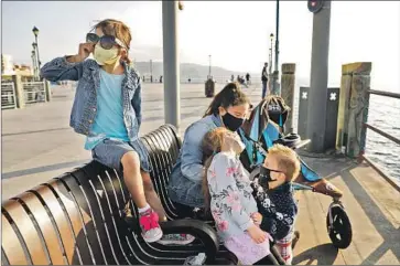  ?? Christina House Los Angeles Times ?? JULIET BROWN, 5, left, visits the Redondo Beach Pier with her siblings Evelyn, 7, and Joshua, 2, center, and their nanny Naomi Collicutt. Universal mask-wearing is seen as crucial to control the spread of the virus.