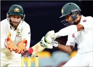  ?? SAEED KHAN/AFP ?? Pakistan’s Asad Shafiq plays a shot as Australian wicketkeep­er Mathew Wade looks on during the fourth day of the day-night Test yesterday.