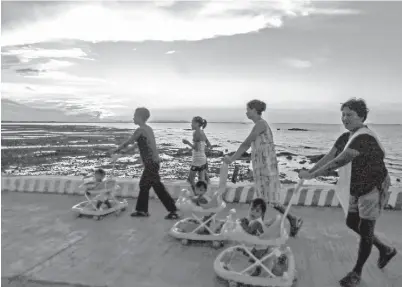  ?? (Rio Leonelle Deluvio) ?? THREE babies on their baby walkers together with their companions stroll along a fishport area in Pilar, Capiz.