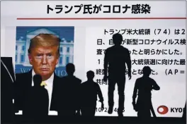  ?? EUGENE HOSHIKO — THE ASSOCIATED PRESS ?? People walk past a screen in Tokyo on Friday showing the news report that President Donald Trump has tested positive for the coronaviru­s.